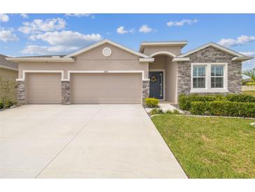 Beautiful single-story home with a manicured lawn, stone accents, and a three-car garage at 32231 Conchshell Sail St, Wesley Chapel, FL 33545