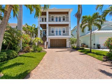 Stunning two-story home with a brick driveway and beautiful landscaping with palm trees against a clear blue sky at 443 18Th Ave, Indian Rocks Beach, FL 33785