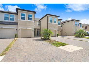 Inviting exterior of home featuring individual garages, neutral stucco, manicured landscaping, and a paver driveway at 29901 Southwell Ln, Wesley Chapel, FL 33543