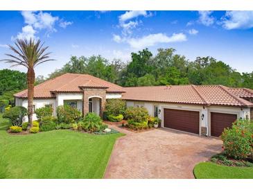 Beautiful single-story home featuring a clay tile roof, lush landscaping, and a brick paved driveway at 14910 Tom Fazio Ct, Tampa, FL 33626