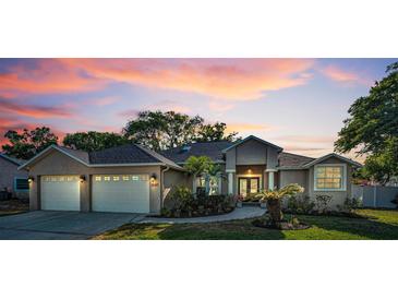 Charming single-story home with a two-car garage, lush landscaping, and a serene sunset backdrop at 3047 Lake Padgett Dr, Land O Lakes, FL 34639