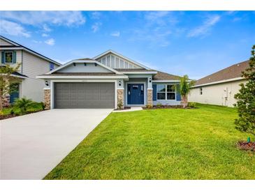 Charming single-story home with a manicured lawn, gray garage door, and blue front door at 16511 66Th E Ln, Parrish, FL 34219
