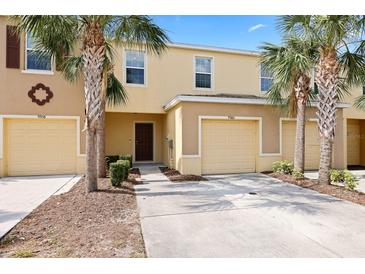 Inviting townhouse exterior featuring a one-car garage, palm trees, and manicured landscaping at 9960 Hound Chase Dr, Gibsonton, FL 33534