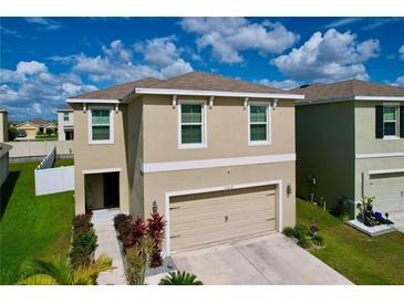 Two-story home with a beige exterior, two-car garage, manicured landscaping, and a blue sky above at 11013 Leland Groves Dr, Riverview, FL 33579