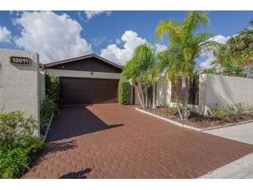 Charming single-Gathering home with a brown two-car garage and brick paved driveway lined with tropical landscaping at 13511 Avista Dr, Tampa, FL 33624