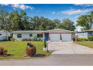 Charming single-story home with a well-manicured lawn, blue door, and a two-car garage under a clear blue sky at 308 Jeanal Pl, Tampa, FL 33612