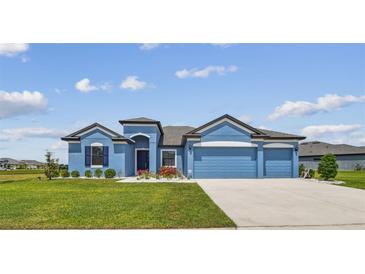 Charming blue single-story home with a well-manicured lawn and a three-car garage at 12710 Wheatgrass Ct, Parrish, FL 34219