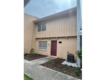Two-story tan home with manicured lawn, garden, and walkway to the maroon front door at 4967 Steel Dust Ln, Lutz, FL 33559