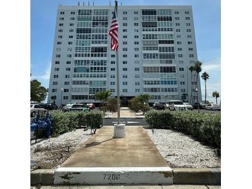 Multi-story condo building with manicured landscaping and an American flag, set against a clear blue sky at 7200 Sunshine Skyway S Ln # 2E, St Petersburg, FL 33711