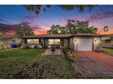 Charming single-story home featuring a well-manicured lawn, inviting fountain, and cozy exterior lighting at 1179 Lazy Lake W Rd, Dunedin, FL 34698
