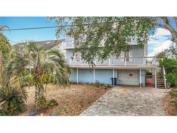 Three-story waterfront home shows balconies, garage access, and tropical landscaping in the yard at 13918 Raie Ave, Hudson, FL 34667