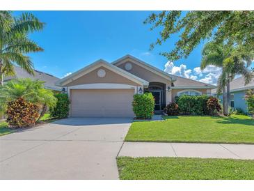 Charming single-story home featuring a lush green lawn, manicured bushes, and a two-car garage on a sunny day at 14510 Haddon Mist Dr, Wimauma, FL 33598