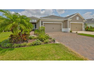 Charming home featuring a brick driveway, a 2-car garage, and beautifully landscaped front yard with tropical plants at 7406 Parkshore Dr, Apollo Beach, FL 33572