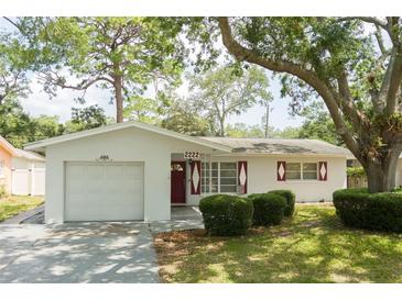 Charming single-story home featuring a one-car garage, red shutters, and lush green landscaping at 2222 Euclid N Cir, Clearwater, FL 33764
