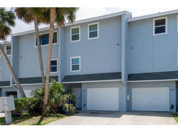 Charming multi-story townhome with a white garage door, tropical landscaping, and light blue exterior at 2643 St Josephs W Dr, Dunedin, FL 34698