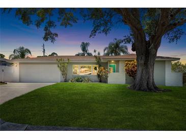 Charming single-story home at dusk with a well-manicured lawn, mature shade tree, and a two-car garage at 1530 Picardy Cir, Clearwater, FL 33755