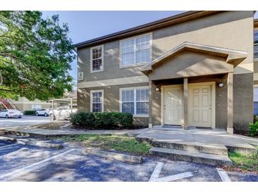 Two-story tan condo with an attached covered parking area and a well-maintained lawn and garden at 5915 Brickleberry Ln # 103, Zephyrhills, FL 33541