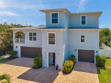 Two-story light blue home boasting a paver driveway, two-car garage, and a balcony at 7115 Bay St, St Pete Beach, FL 33706