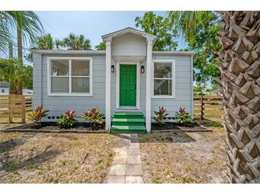 Charming cottage-style home featuring a light-gray exterior, green door, and landscaped front yard at 1527 E Lake Ave, Tampa, FL 33610