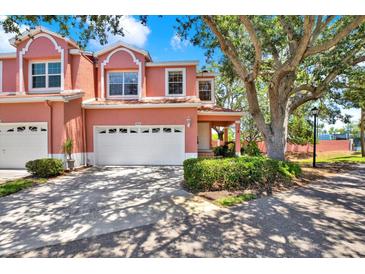 Charming pink townhouse featuring a two-car garage and lush landscaping at 14561 El Paseo Dr, Seminole, FL 33776