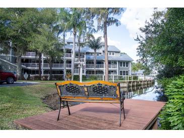 Scenic view of a multi-story condo building overlooking a tranquil canal with lush landscaping and a relaxing dockside bench at 2533 Dolly Bay Dr # 203, Palm Harbor, FL 34684