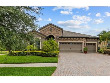 Charming home featuring a three-car garage, manicured lawn, and stone facade, and a brick-paved driveway at 1002 Cavour Ct, Brandon, FL 33511