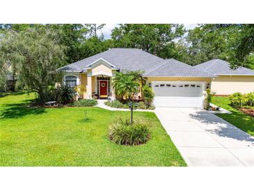 Lovely home with a well-maintained lawn, mature trees, and a three-car garage, and a welcoming red door at 12435 Oak St, San Antonio, FL 33576