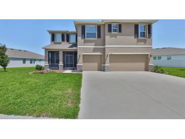 Inviting two-story home featuring a well-manicured lawn and attached two-car garage with tan paint and black shutters at 11924 Brighton Knoll Loop, Riverview, FL 33579