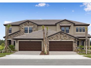 A beautiful townhouse featuring a stone facade and two-car garage with brick paver driveway at 35617 Stableton Lane, Zephyrhills, FL 33541