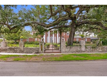 Brick home behind wall with wrought iron fence and gate, large oak tree hangs over the front at 5002 S Shore Crest Cir, Tampa, FL 33609
