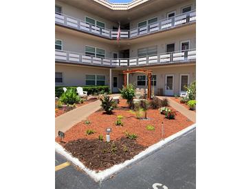Exterior view of a multi-story building with landscaped courtyard, white Adirondack chairs, and walkways at 5530 80Th N St # A306, St Petersburg, FL 33709