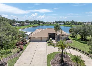 Beautiful lakefront home featuring a circular driveway, mature landscaping, and an oversized three-car garage at 8827 Scout Lake Ct, New Port Richey, FL 34654