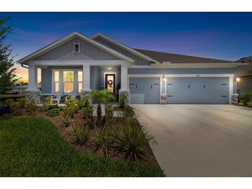 Charming single-story home with a three-car garage, inviting front porch, and beautifully landscaped yard at dusk at 8916 Windlass Cv, Parrish, FL 34219