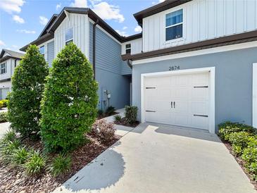 Two-story townhome features a white garage door, blue siding, and manicured landscaping at 2874 Deer Pine Trl, Land O Lakes, FL 34638