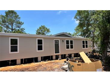 New single-story home featuring a neutral exterior, white-trimmed windows, and a front door, set against a bright blue sky at 10040 Lake Dr, Weeki Wachee, FL 34613