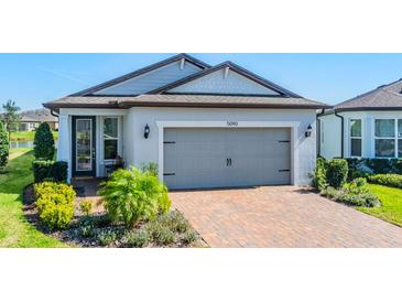 Attractive home featuring a brick driveway, a gray two-car garage door, and manicured landscaping at 5090 Caravel Pt, Land O Lakes, FL 34638