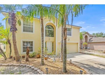 Charming two-story home featuring a two car garage, light yellow paint and mature landscaping and palm trees at 10311 Frog Pond Dr, Riverview, FL 33569
