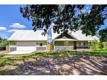 Charming home with light green siding, stone accents, a metal roof, and a detached garage at 16930 Sweetwater Rd, Dade City, FL 33523