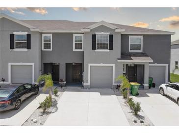 A row of gray townhomes with driveways and minimalistic landscaping featuring palm trees, small bushes, and white gravel at 33062 Frosted Clover Way, Wesley Chapel, FL 33545
