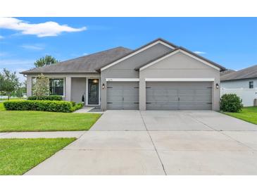 Beautiful single-story home with a manicured lawn, gray facade, and three-car garage at 6670 Paden Wheel St, Zephyrhills, FL 33541