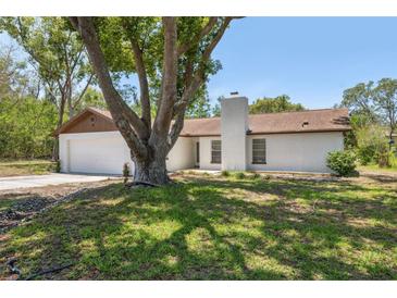 Charming single-story home features a brick exterior, chimney, attached garage, and mature trees in the front yard at 1555 Newhope Rd, Spring Hill, FL 34606