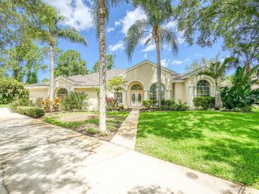 Charming single-story home featuring a manicured lawn, elegant arched windows, and lush tropical landscaping at 3910 Saywood Ct, Palm Harbor, FL 34685