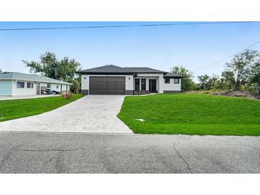 Modern single-story home featuring a two-car garage, a well-manicured lawn, and a brick-paved driveway at 7054 Rosemont Dr, Englewood, FL 34224