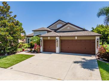 Charming home showcasing a three-car garage, manicured lawn, and beautifully landscaped garden beds at 347 Cockle Shell Loop, Apollo Beach, FL 33572