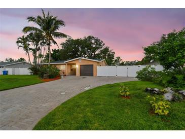 Single-story home at dusk featuring a well-maintained lawn, brick driveway, and privacy fence at 4400 Helena Ne St, St Petersburg, FL 33703