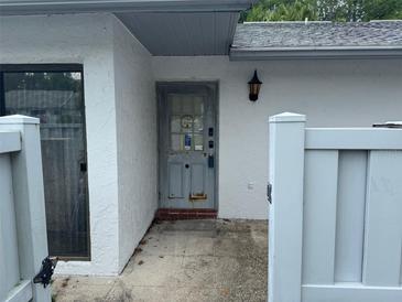 A gray door offers entry to this home, framed by a white textured wall and shadowed by an elegant outdoor light at 1371 Pine Ridge E Cir # B8, Tarpon Springs, FL 34688