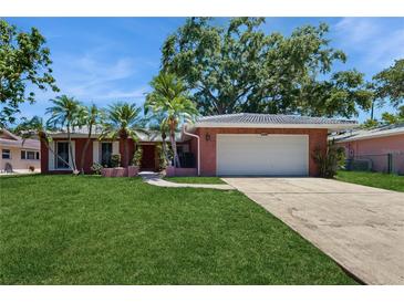 Charming single-story brick home with a lush green lawn, palm trees, and a two-car garage at 2138 Viola Dr, Clearwater, FL 33764