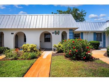 Charming home exterior featuring white walls, a metal roof, arched doorways, and vibrant landscaping at 4229 Glissade Dr, New Port Richey, FL 34652