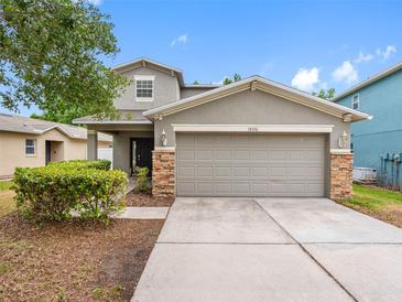 Charming gray two-story home with a two-car garage, stone accents, manicured landscaping, and concrete driveway at 18320 Snowdonia Dr, Land O Lakes, FL 34638