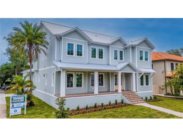 Stunning two-story light blue home with a metal roof, inviting front porch, and lush landscaping at 4311 W Sevilla St, Tampa, FL 33629